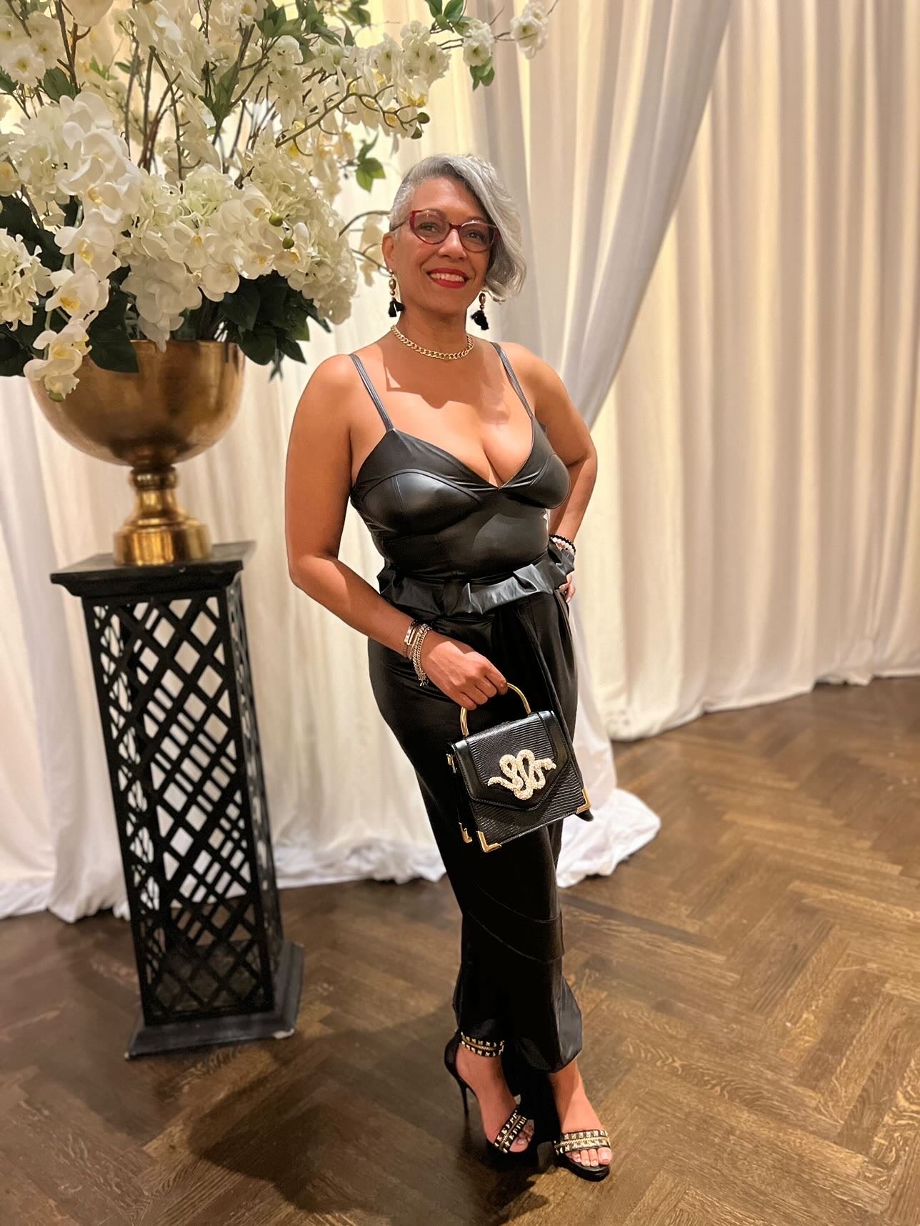 Model wearing the Suspense sleeveless jumpsuit featuring a fitted silhouette, removable vegan leather belt, faux pockets, and ankle straps for a structured, statement look.